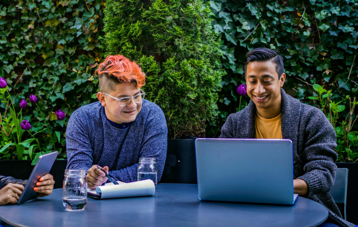 Two professionals collaborating outdoors with a laptop and tablet, surrounded by greenery